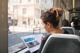 Young woman in a Marseille café, reviewing handwritten notes and local job ads, with coffee and city street visible through the window, soft natural daylight creating a thoughtful atmosphere.